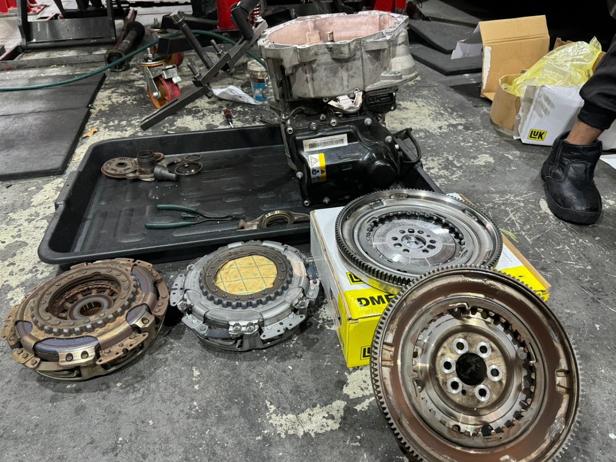 A clutch and dual mass flywheel job laid out on the floor, old and new clutch plates, two flywheels and LuK part boxes