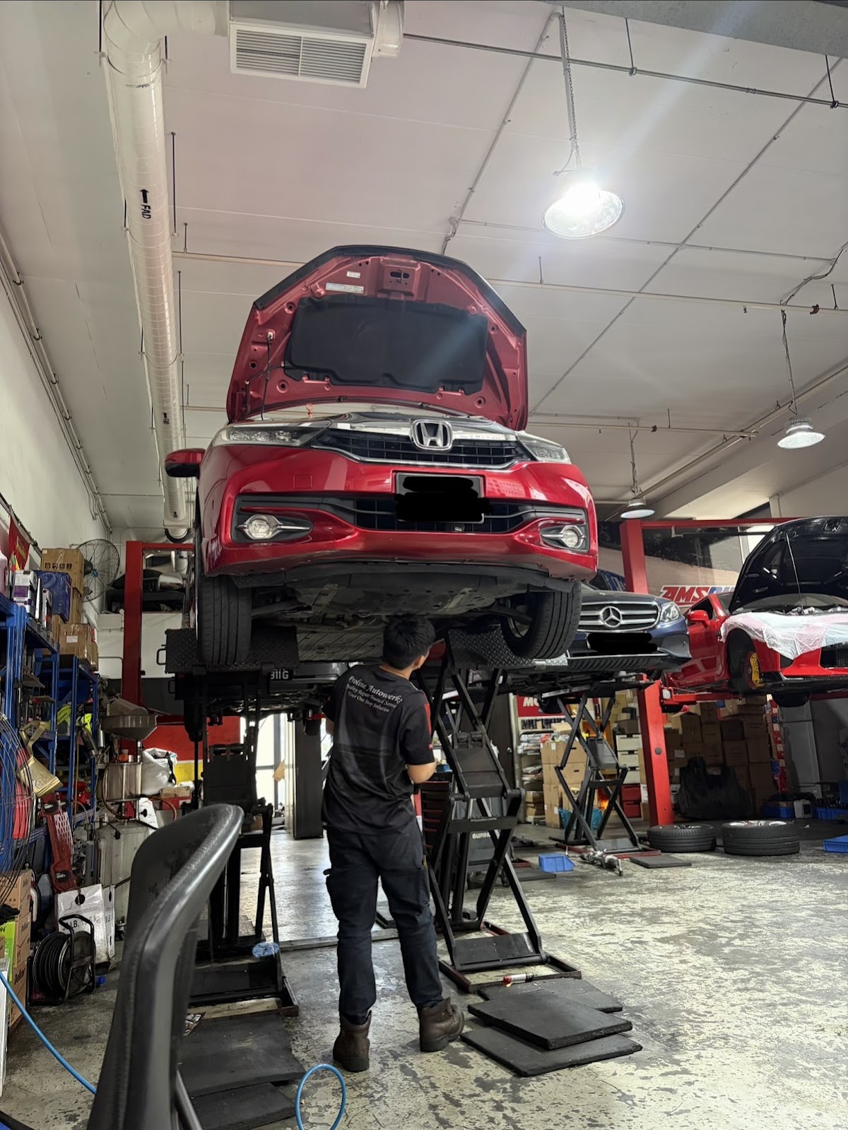 A red Honda raised on a scissor lift with a technician in a Proline Autowerks polo working underneath it