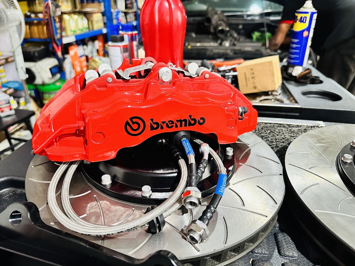 A red Brembo big brake caliper on a slotted rotor with braided stainless brake lines, on a workbench