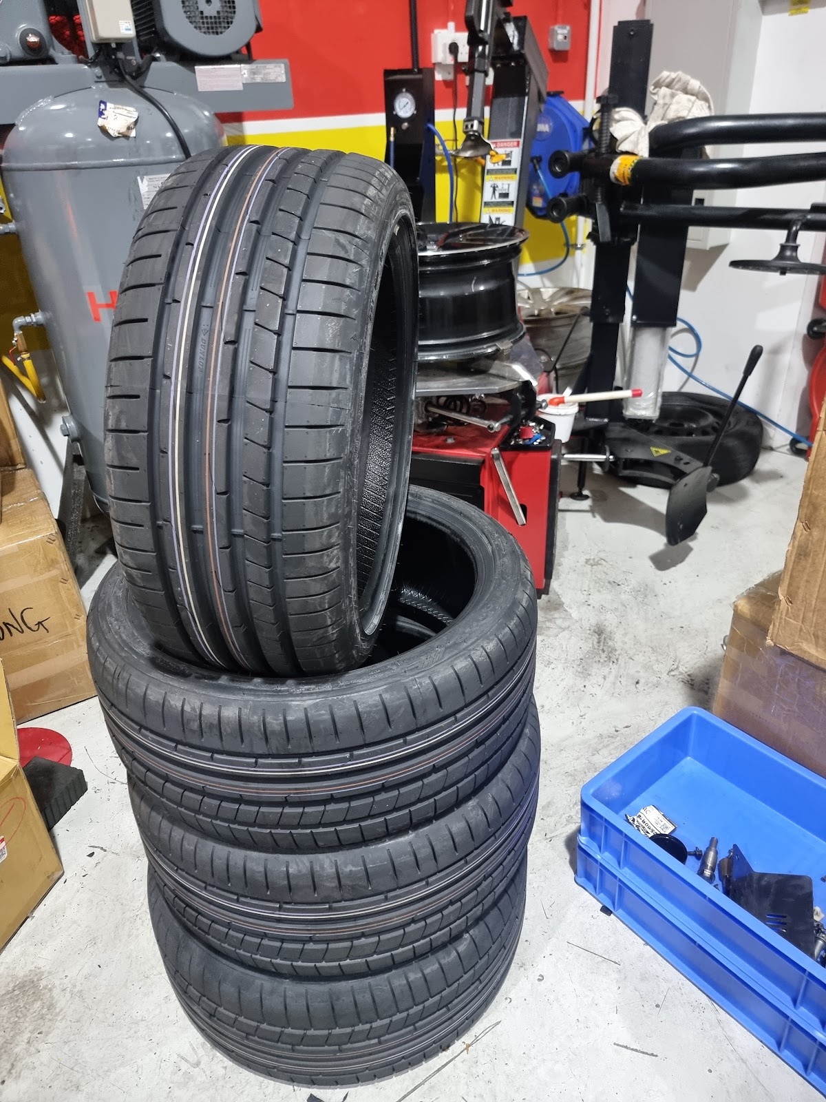 Four performance tyres stacked beside a tyre changing machine and wheel balancer