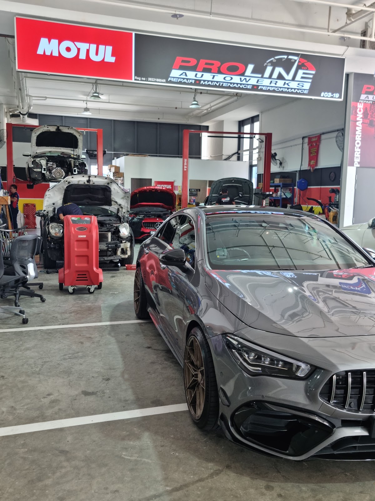 A grey Mercedes-AMG CLA on bronze wheels parked under the Motul and Proline Autowerks signboard, with an Audi being serviced behind it