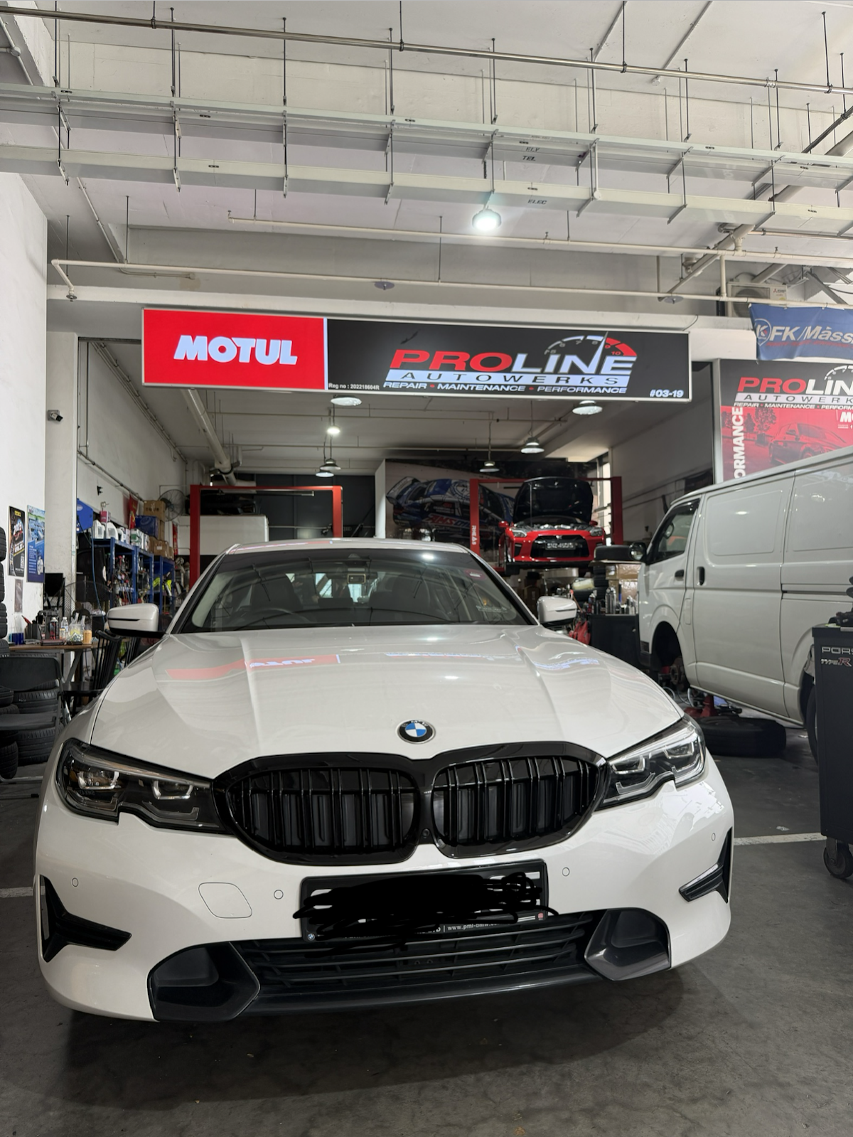 A white BMW 3-series inside the workshop under the Motul and Proline Autowerks signboard, a red Honda Civic Type R behind it